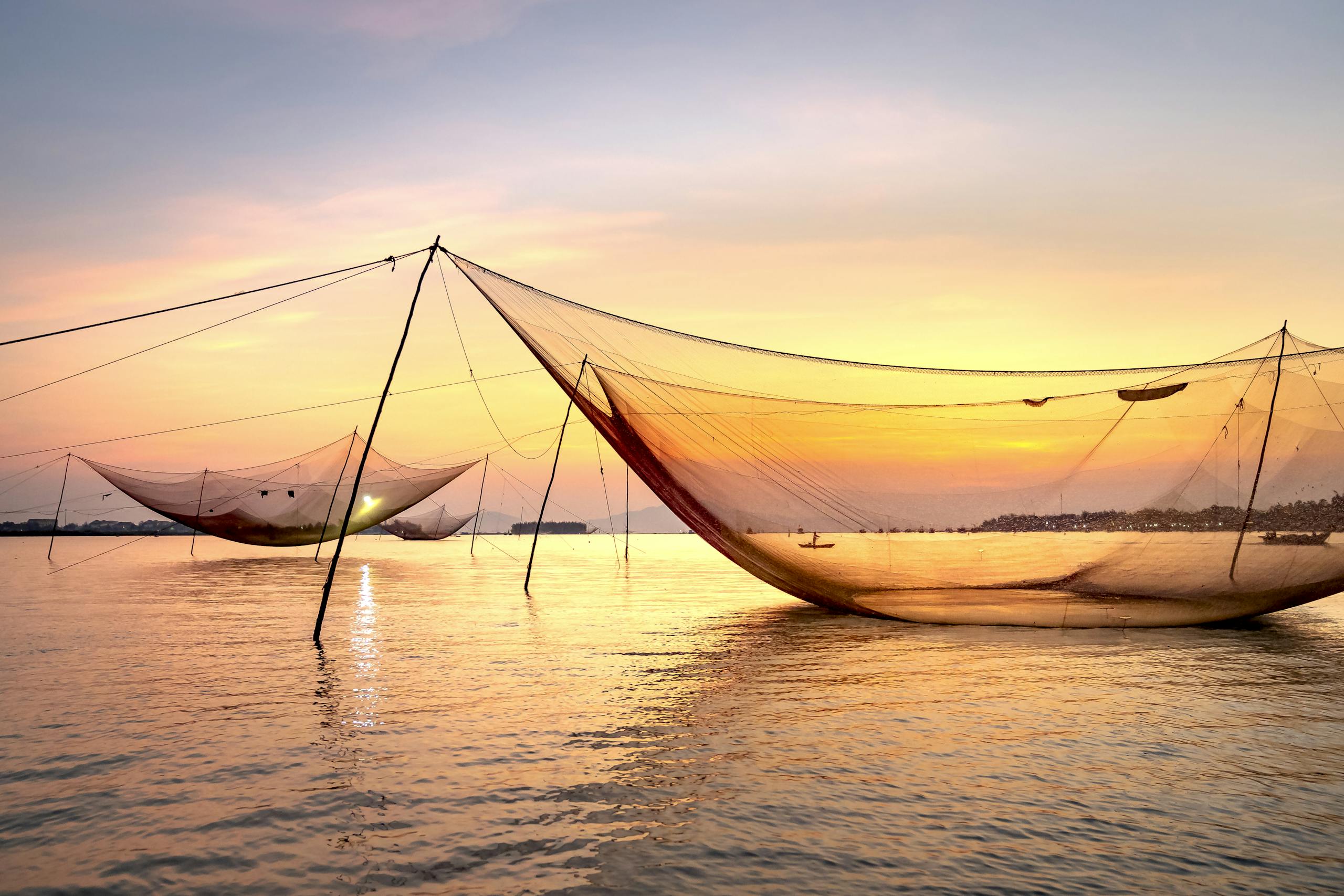 Special big fishing nets cast on sea surface against bright sundown sky in coastal area on summer evening in nature