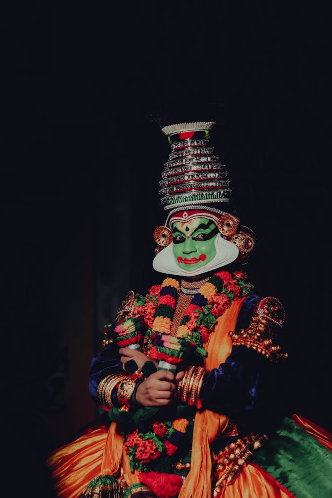 Vibrant portrait of a Kathakali performer in traditional attire showcasing intricate makeup and costume against a dark background.